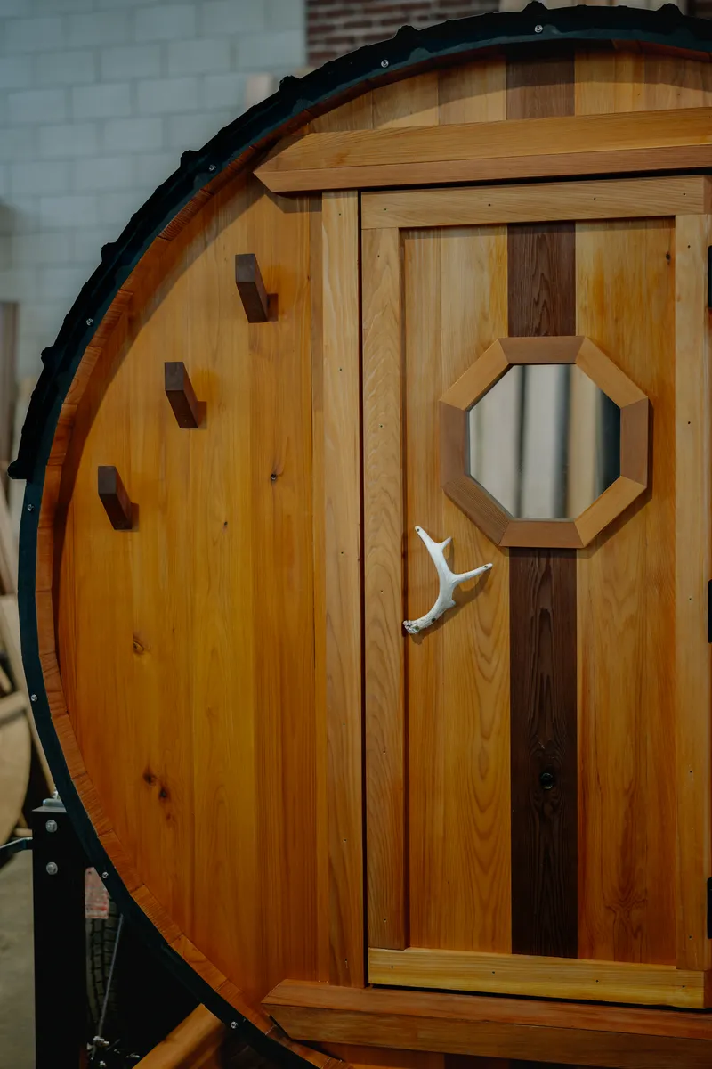 Barrel sauna front wall with antler door handle and dark walnut wall hooks on natural cedar